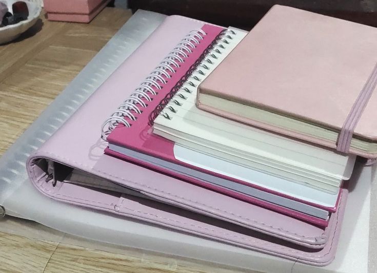 a pink binder with several notebooks stacked on top of each other