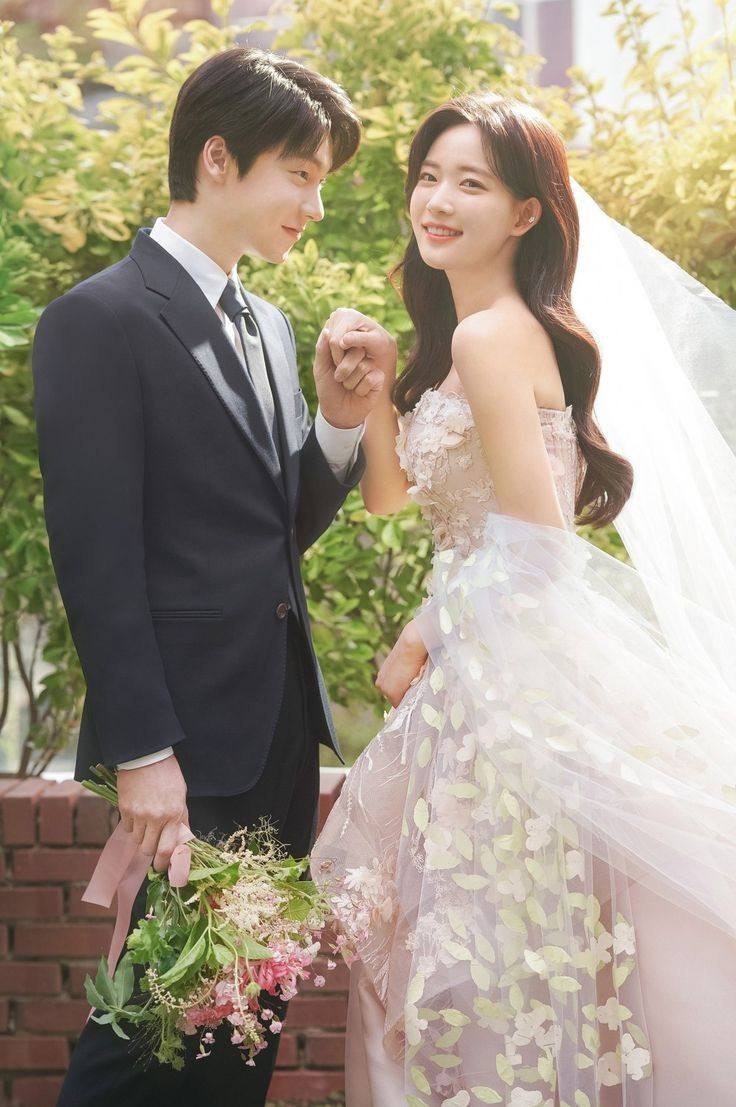 a man and woman standing next to each other in front of some trees holding hands