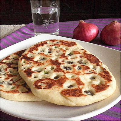 two pita breads on a plate next to a glass of water and some onions