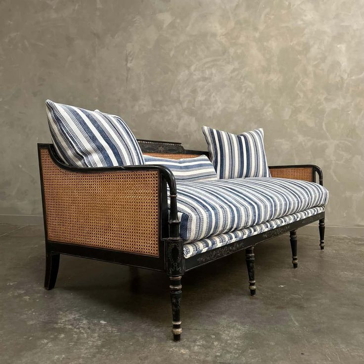 a striped couch sitting on top of a wooden floor next to a gray wall with two blue and white pillows