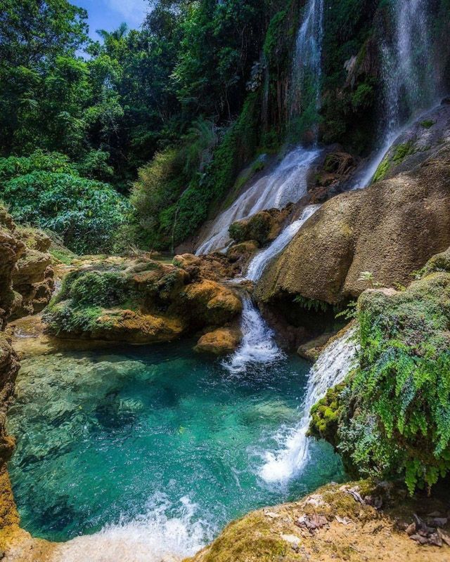 a small waterfall in the middle of a river with blue water and green vegetation on both sides