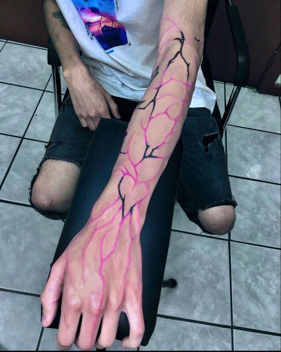 a man is sitting on the floor with his arm wrapped in pink lightning bolt tattoos