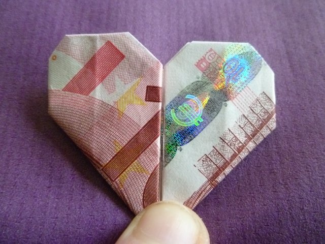 a hand holding an origami heart made out of money on a purple surface