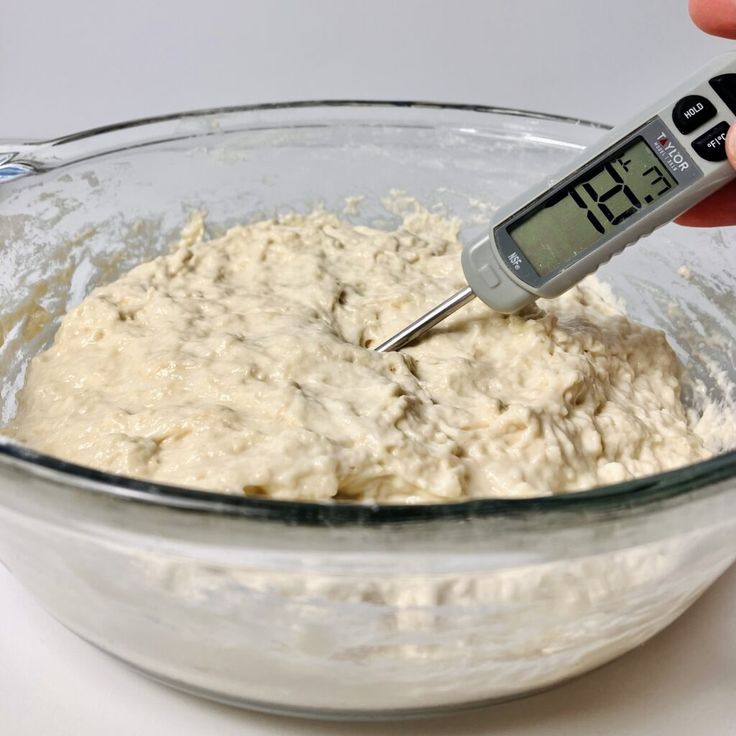 a person using a digital thermometer to measure food in a glass mixing bowl