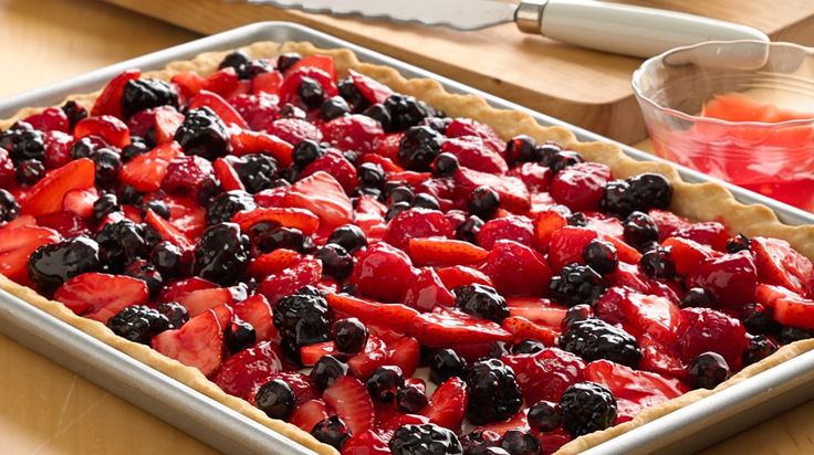 a pie with strawberries and blueberries in it sitting on a table next to a knife