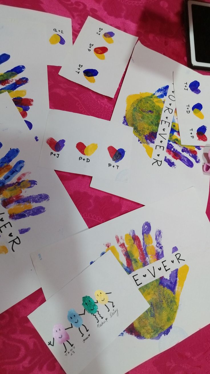 several children's handprints are laid out on a pink table with a cell phone