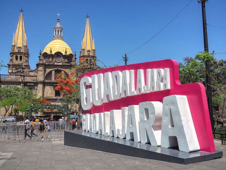 there is a large sign that says guadalajara in front of the cathedral and clock tower