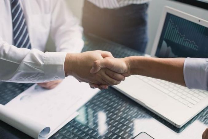 two people shaking hands in front of laptops on a desk with papers and notebooks