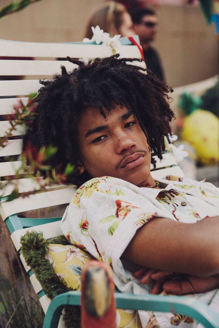 a young man with dreadlocks sitting on a bench in front of other people