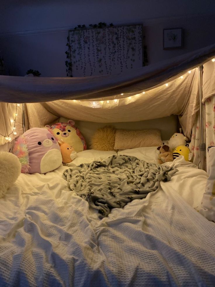 there is a bed with many stuffed animals on it and lights strung around the headboard