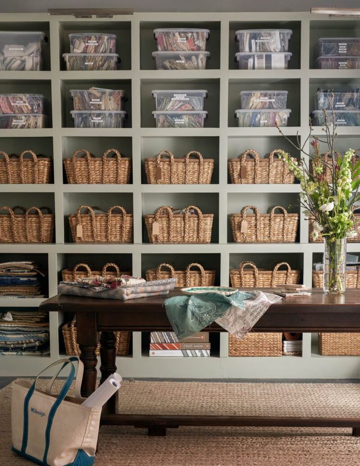 a room filled with lots of books and baskets next to a wooden table in front of a book shelf