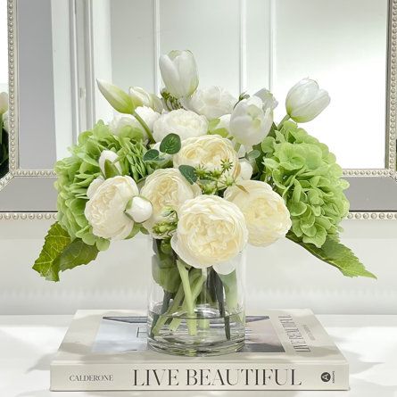 a vase filled with white flowers sitting on top of a table next to a mirror