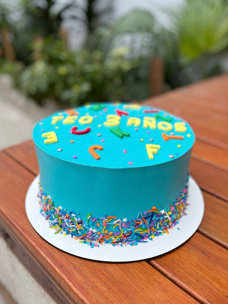 a blue birthday cake with sprinkles on a wooden table in the background