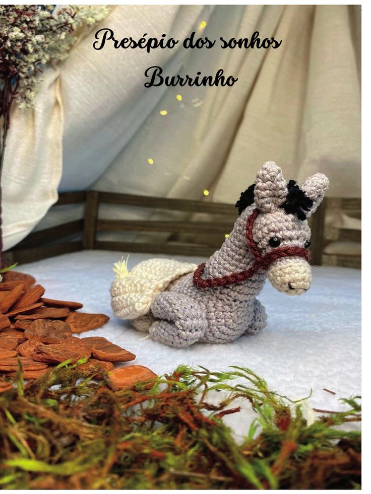 a crocheted horse sitting on top of a bed next to dry grass and flowers