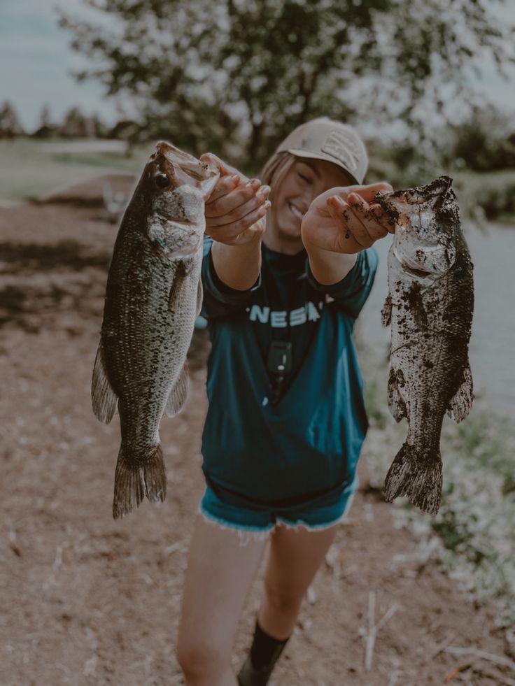 a young boy holding two fish in one hand while standing on a dirt path next to water