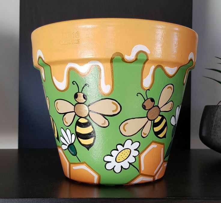 a pot with bees painted on it sitting on a table next to a planter