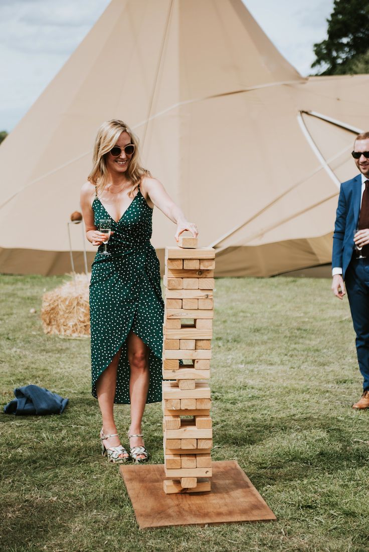 a woman in a green dress standing next to a wooden block tower on top of grass