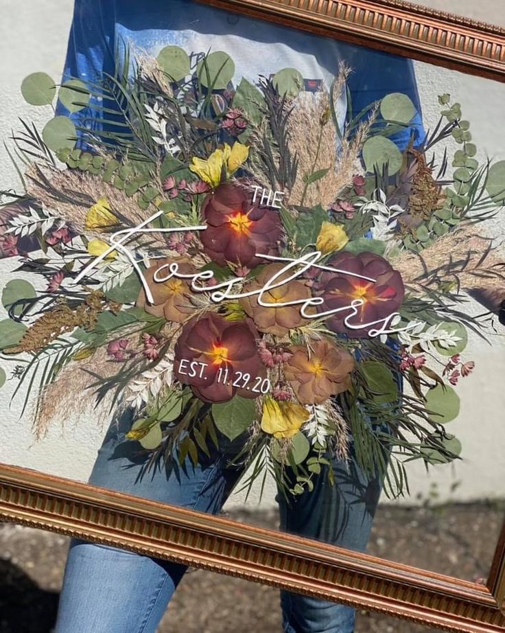 a woman holding a framed photo with flowers in it