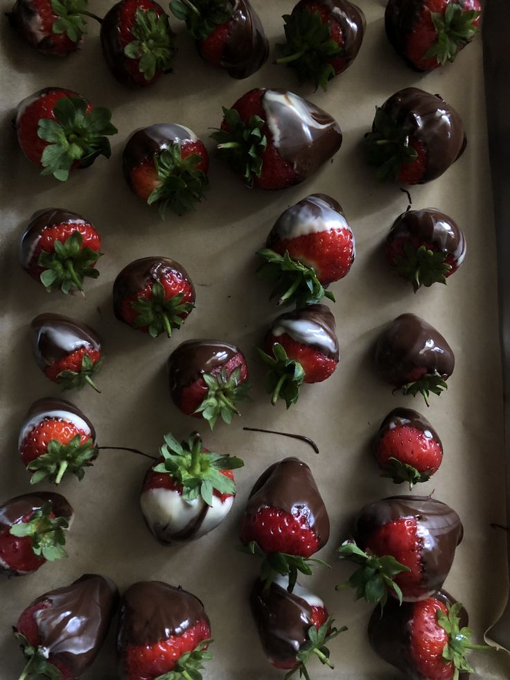 chocolate covered strawberries are arranged on a baking sheet with green leaves and sprigs