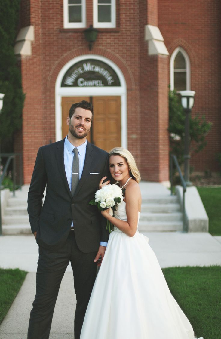 a bride and groom standing in front of a church with their arms around each other