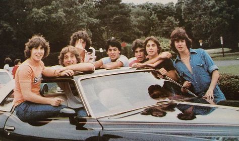 a group of young men sitting on top of a car in front of trees and bushes