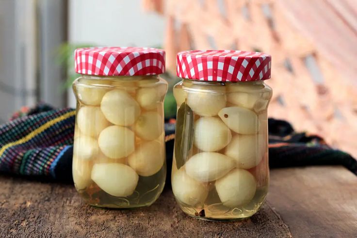 two jars filled with pickles sitting on top of a wooden table next to a cloth