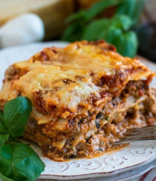 a white plate topped with lasagna casserole covered in sauce and cheese