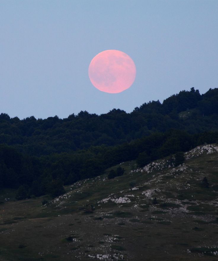 the full moon is setting over some hills