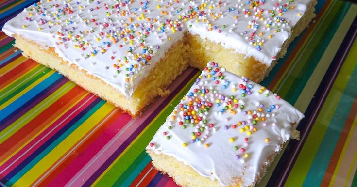 a cake with white frosting and sprinkles on a colorful table cloth