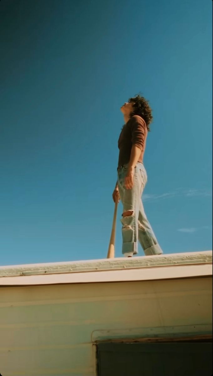 a man walking on top of a roof with a baseball bat in his right hand