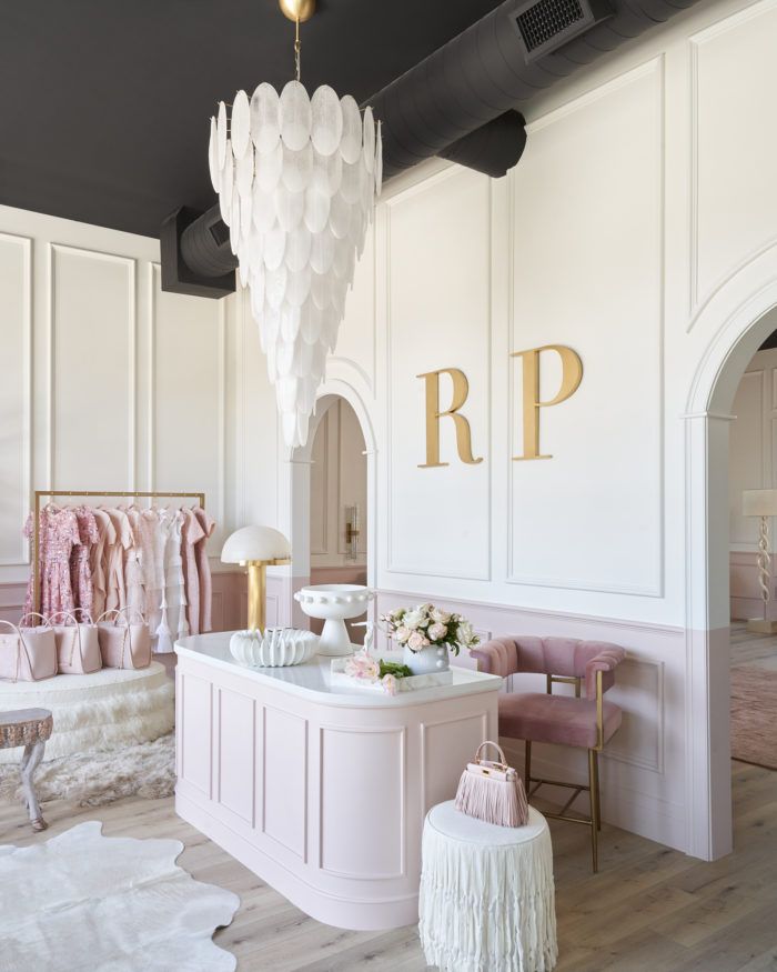 the interior of a boutique with pink and white furniture, chandelier, and dressing area