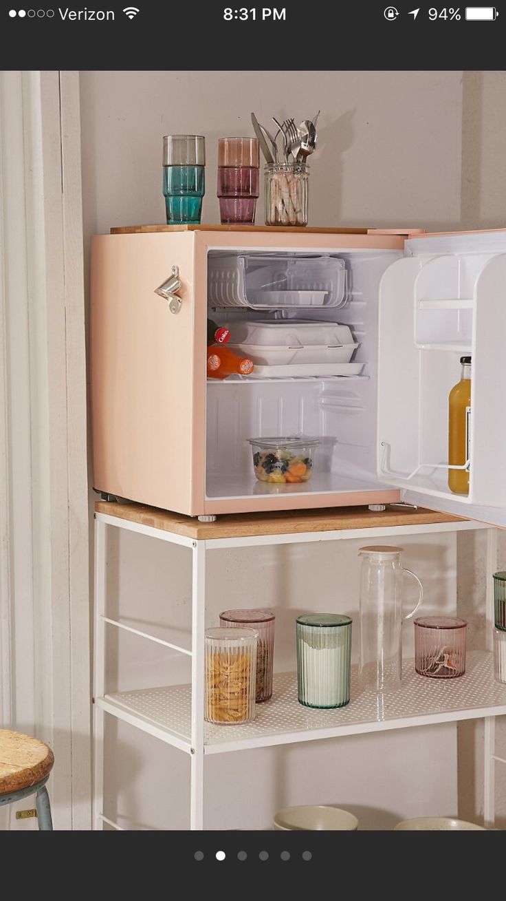 an open refrigerator sitting on top of a white shelf next to cups and bowls in front of it