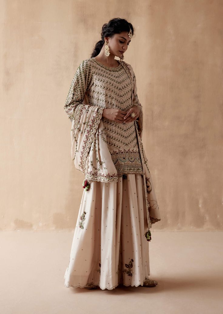 Editor's Note Introducing an exquisite ivory kurta adorned with intricate floral thread embroidery, elegantly highlighted with various embellishments. This captivating ensemble is paired with a stunning sharara and a heavily embroidered dupatta, creating a luxurious and regal look perfect for grand occasions or festive celebrations. The combination of the intricate embroidery, embellishments, and the richness of the dupatta adds an opulent touch, making this outfit a statement of classic eleganc Beige Semi-stitched Sharara For Eid, Cream Anarkali Set With Resham Embroidery In Chinon, Semi-stitched Sharara With Chikankari Embroidery, Reception Straight Kurta Palazzo Set In Chinon, Designer Cream Chinon Anarkali Set, Chinon Palazzo Set For Reception With Straight Kurta, Festive Cream Salwar Kameez In Chinon Fabric, Festive Cream Chinon Salwar Kameez, Cream Anarkali Set With Intricate Embroidery In Georgette