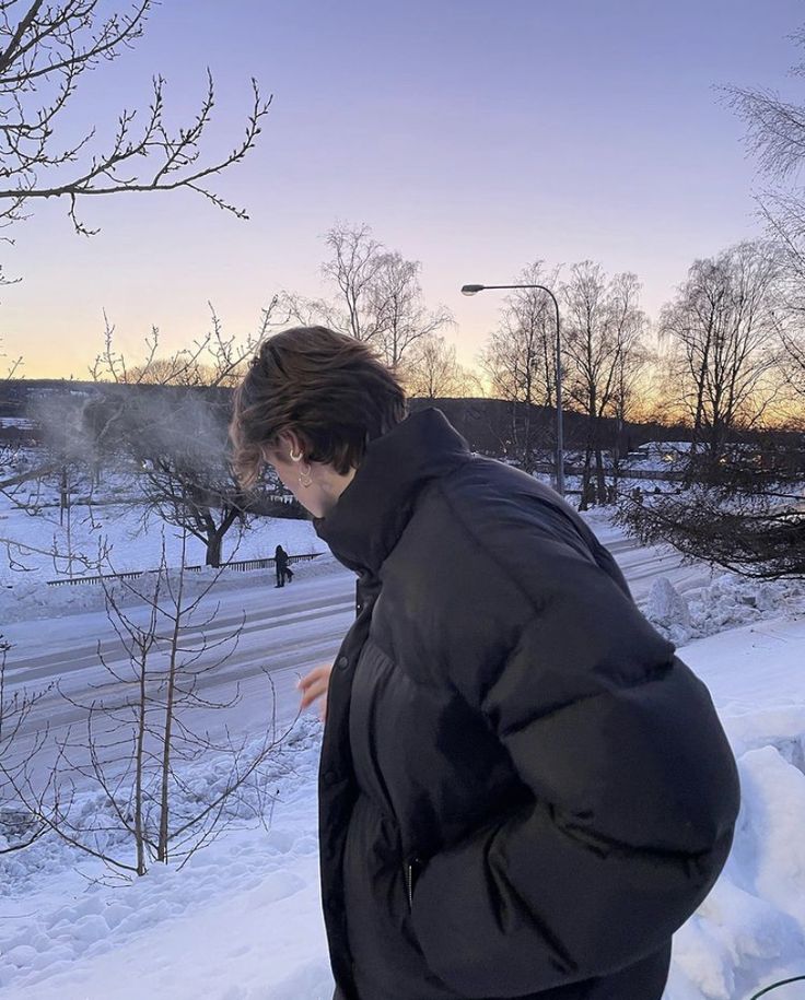 a man standing in the snow looking down at something on his hand while wearing a black jacket