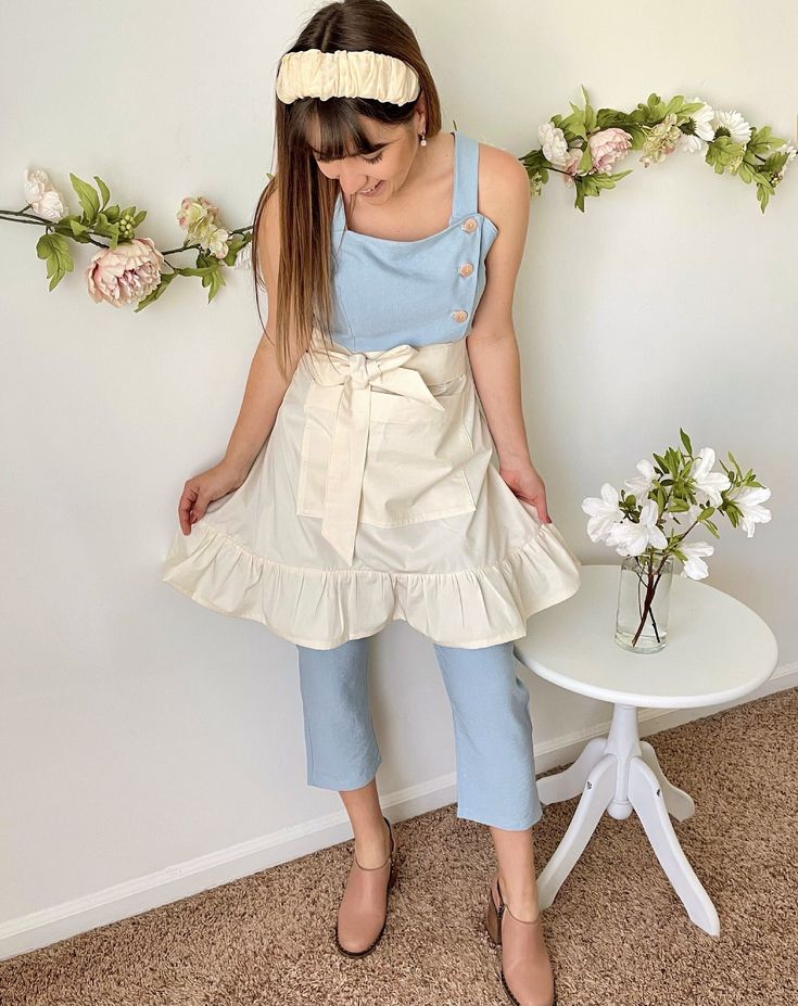 a woman standing next to a white table with flowers on it and wearing a blue top