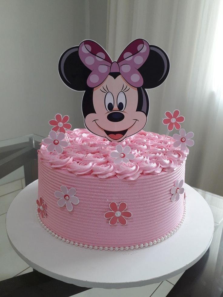 a minnie mouse cake with pink frosting and flowers on top, sitting on a table