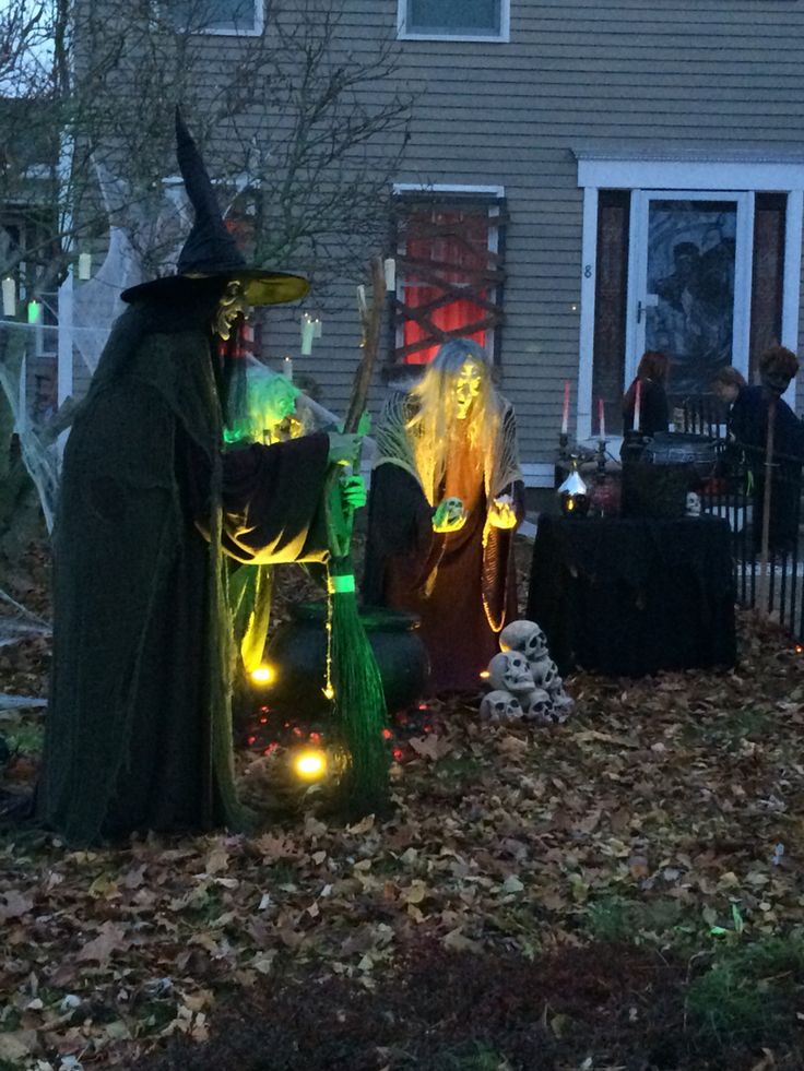 two people dressed as witches in front of a house with halloween decorations on the lawn