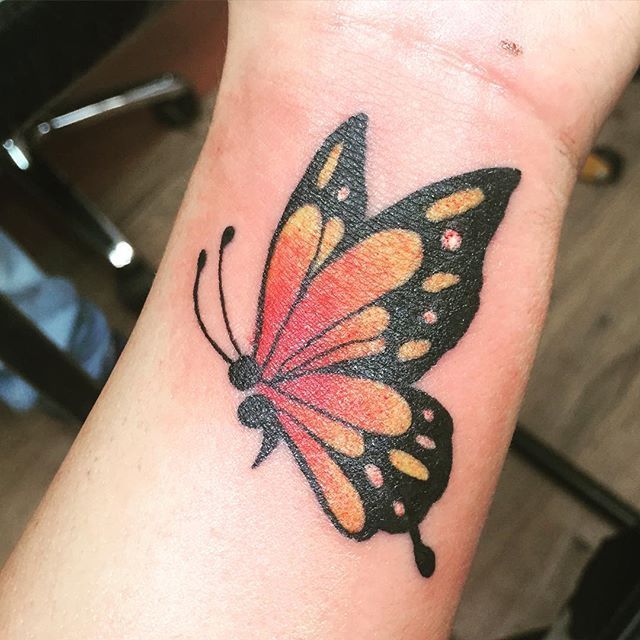 a small butterfly tattoo on the wrist is shown in red, yellow and black colors