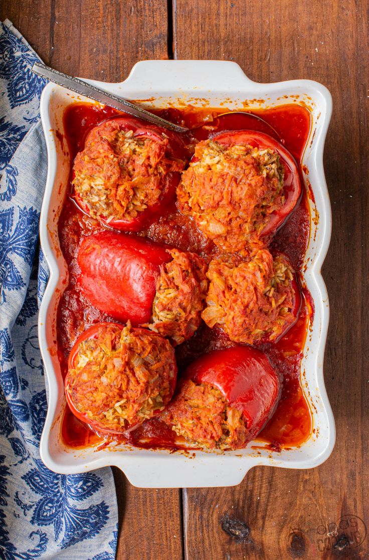 stuffed peppers in a casserole dish on a wooden table with a blue and white towel