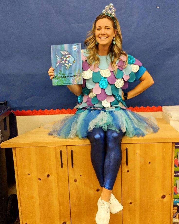 a woman sitting on top of a wooden cabinet holding a book in her hand and smiling