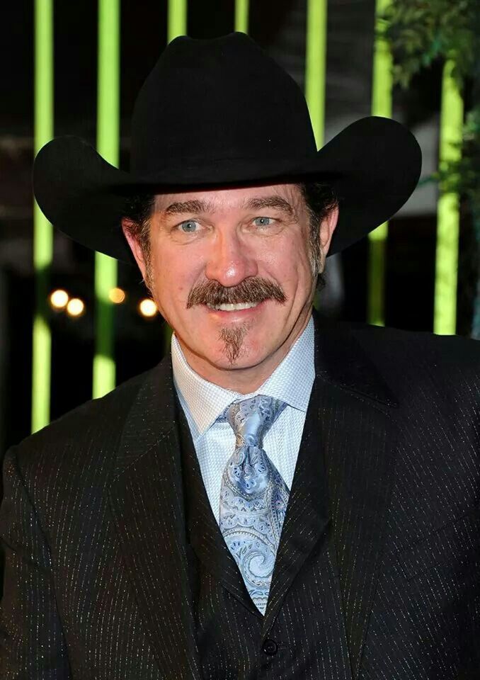 a man in a suit and tie wearing a black hat with a moustache