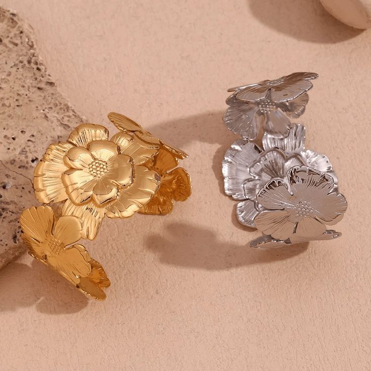 Add a touch of playfulness to your outfit with our Flower Cluster Cuff! This statement cuff bracelet features a cluster of beautiful flowers, bringing a whimsical and unique element to any look. Perfect for those who don't take themselves too seriously and like to add a bit of fun to their style. DETAILS & SIZE Finish: 18K gold plate Material: Stainless Steel Measurements: Diameter: 2.2"; Width: 1.5" Weight: 35 grams Waterproof, tarnish-resistant, and nickel free Shop Bracelets to curate your arm stack! Adjustable Flower Cuff Bracelet For Spring, Spring Wedding Bangle Bracelets, Spring Metal Cuff Jewelry, Spring Flower Metal Bracelets, Spring Flower-shaped Metal Bracelets, Spring Wedding Metal Bracelets, Adjustable Flower Ring For Party, Spring Cuff Bracelet Suitable For Gifting, Arm Stack