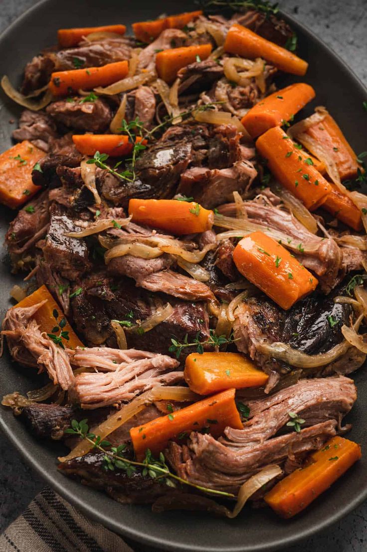 a plate with meat, carrots and onions on it next to a fork in the bowl