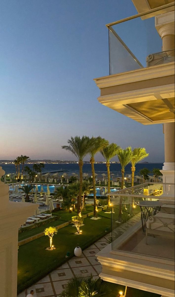 an outside view of a resort with lawn and palm trees at dusk, looking out over the ocean