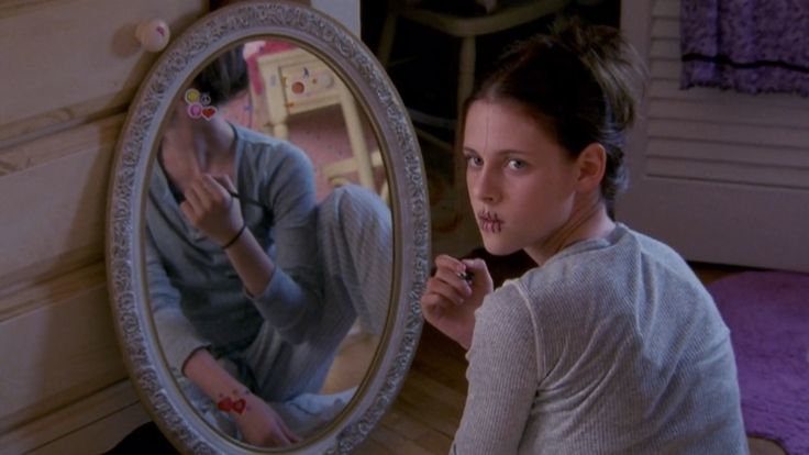 a young woman brushing her teeth in front of a mirror with the reflection of herself