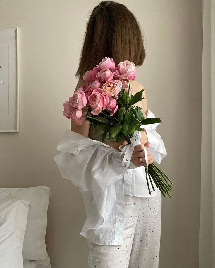 a woman holding a bouquet of pink roses in her hands and looking at the wall