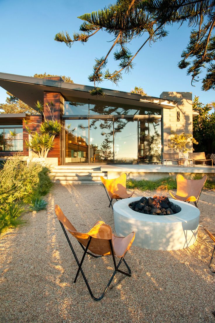 an outdoor fire pit in the middle of a gravel area with chairs and tables around it