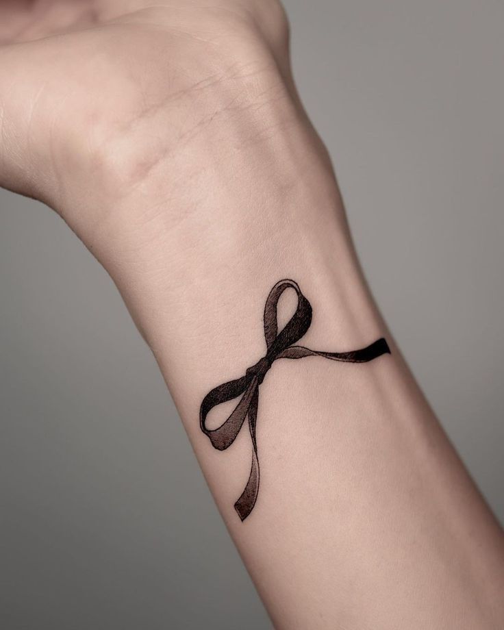 a woman's wrist with a black ribbon tattoo on the left side of her arm