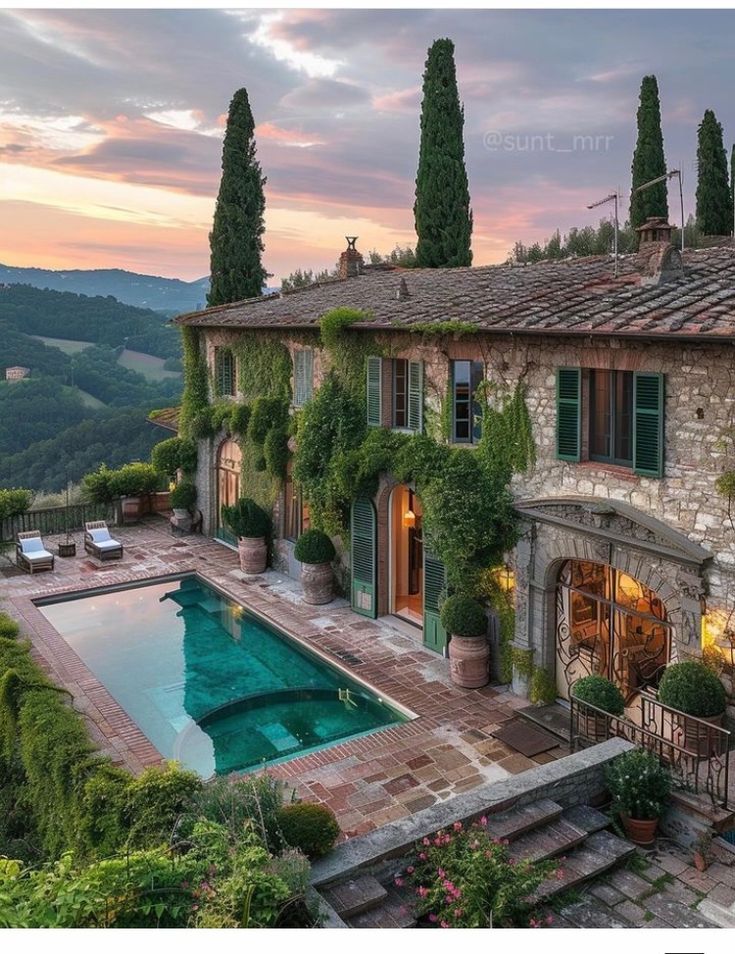 an outdoor swimming pool in front of a stone house with trees and bushes around it