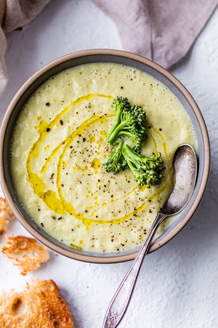 a bowl filled with broccoli and cheese next to crackers on a white surface